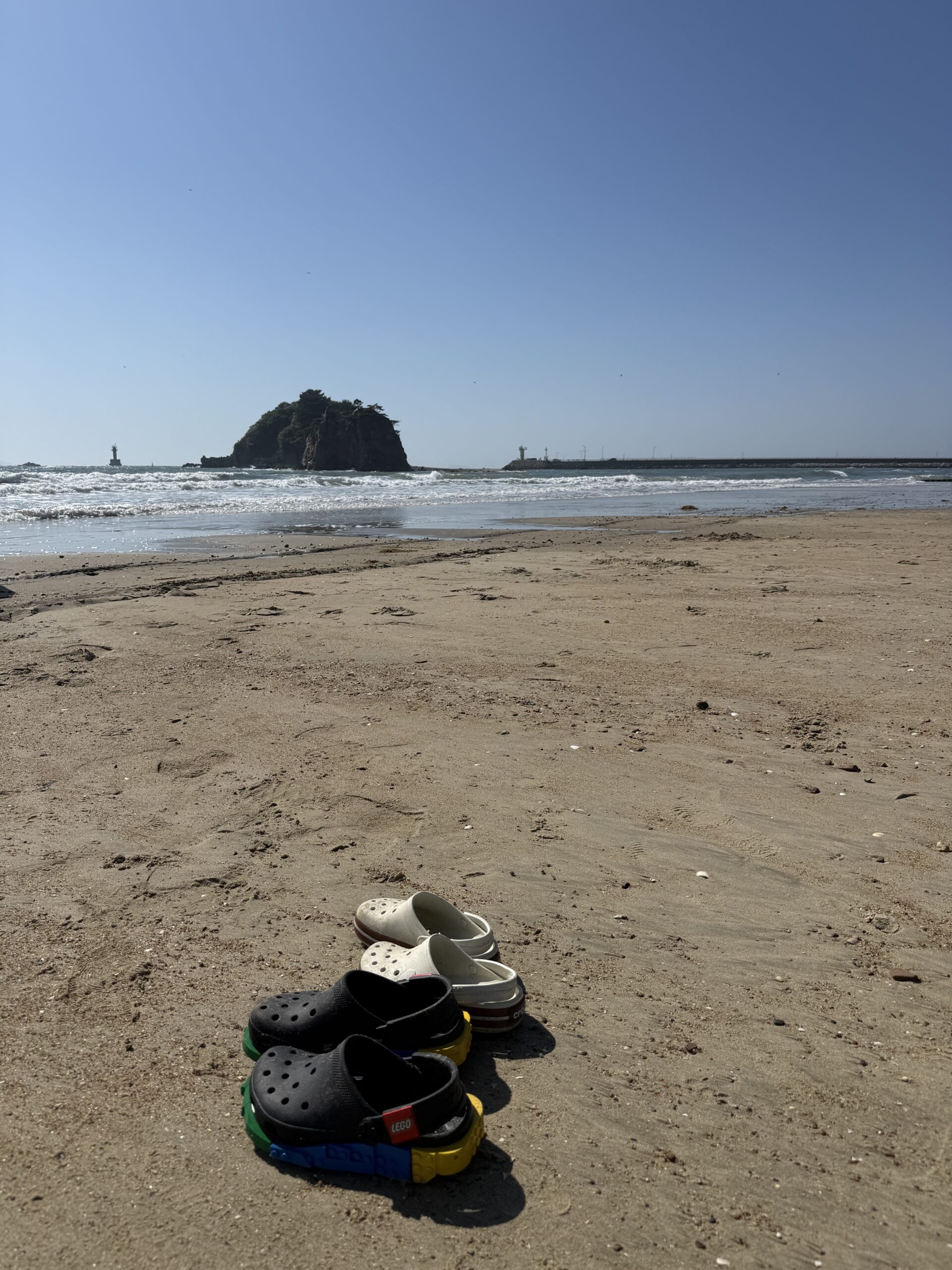 Four pairs of Crocs lined up on Kkotji Beach sand for family stop