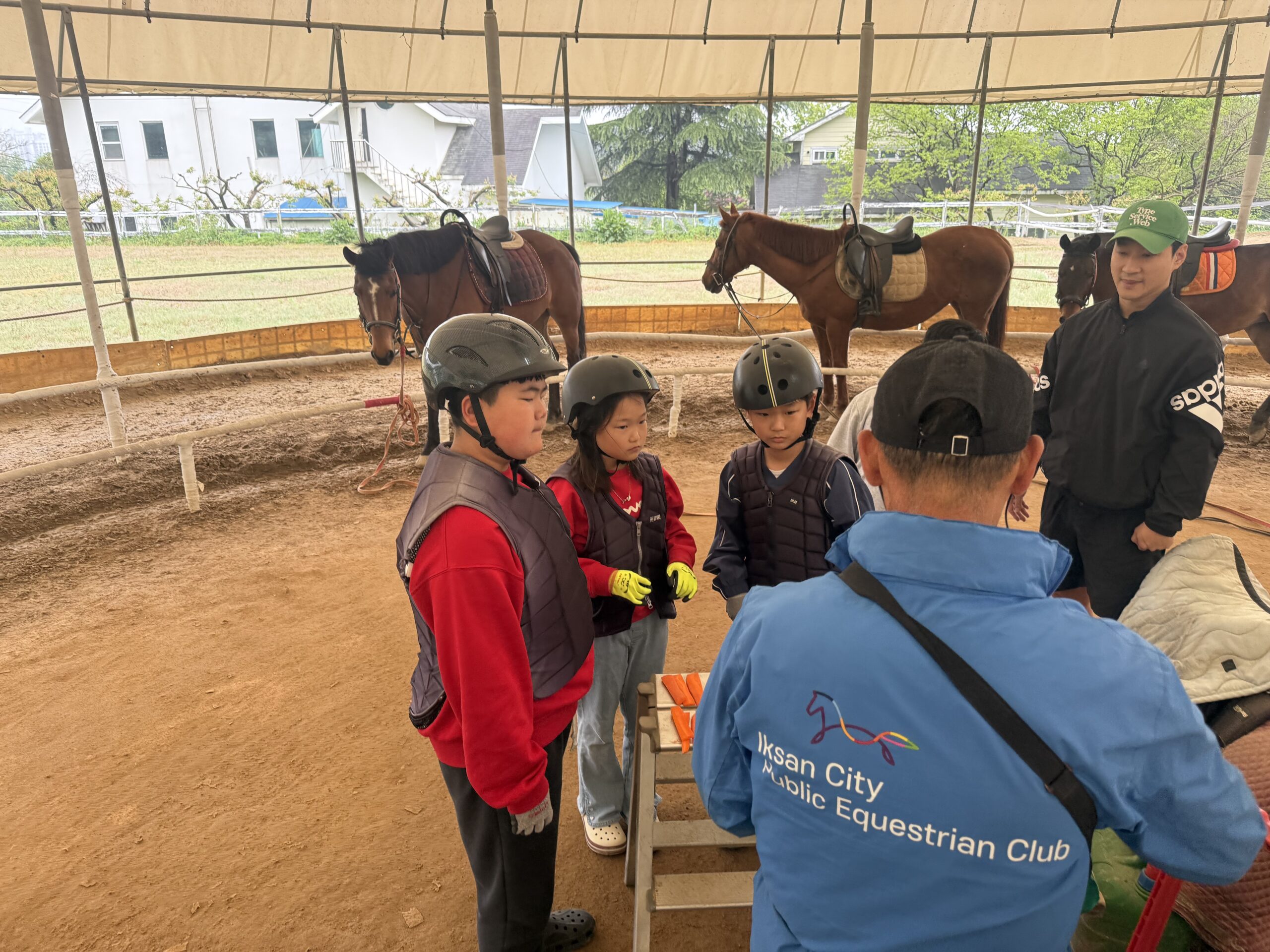 Horseback riding coach briefing kids in helmets and vests at Naepo Camping Square