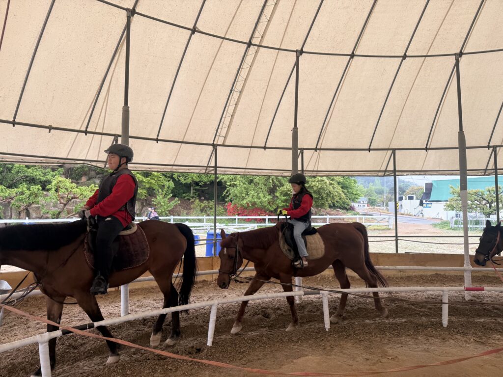 Two children riding horses side by side in lunge line lesson at Naepo Camping Square