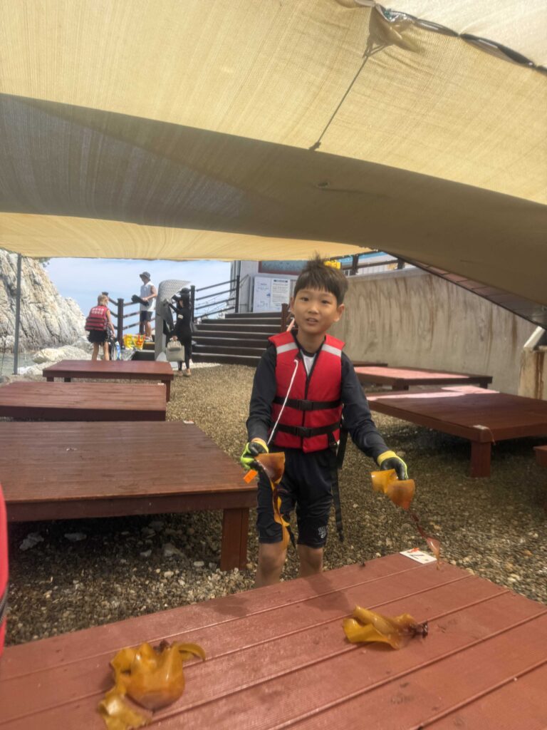 Boy in a life jacket holding a sea squirt found while snorkeling at Jangho Beach with kids