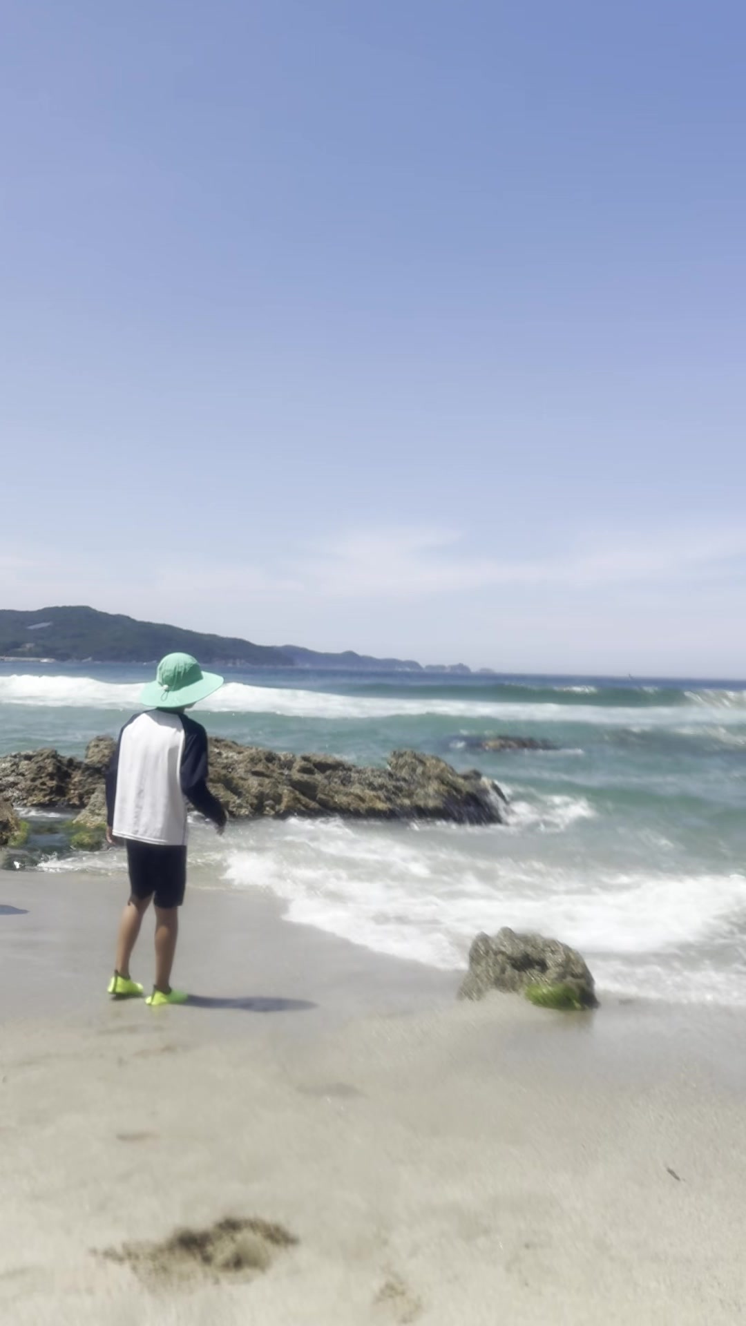 Boy in a green hat facing the breaking waves at Munam Beach Samcheok