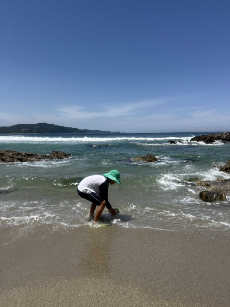 Child digging clams in the wet sand as a wave rolls in at Munam Beach Samcheok