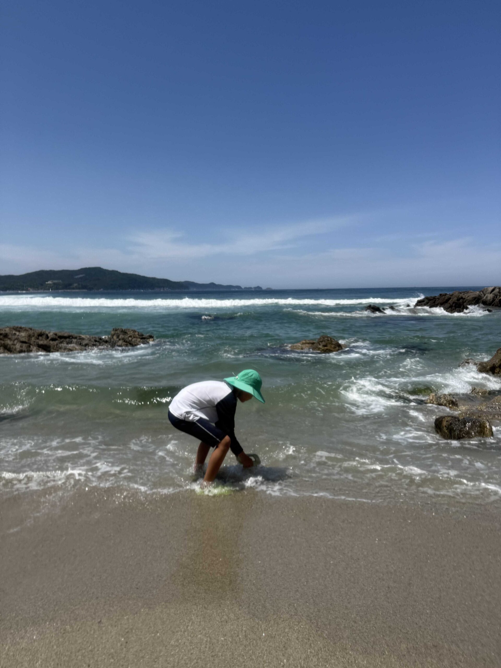 Child digging clams in the wet sand as a wave rolls in at Munam Beach Samcheok