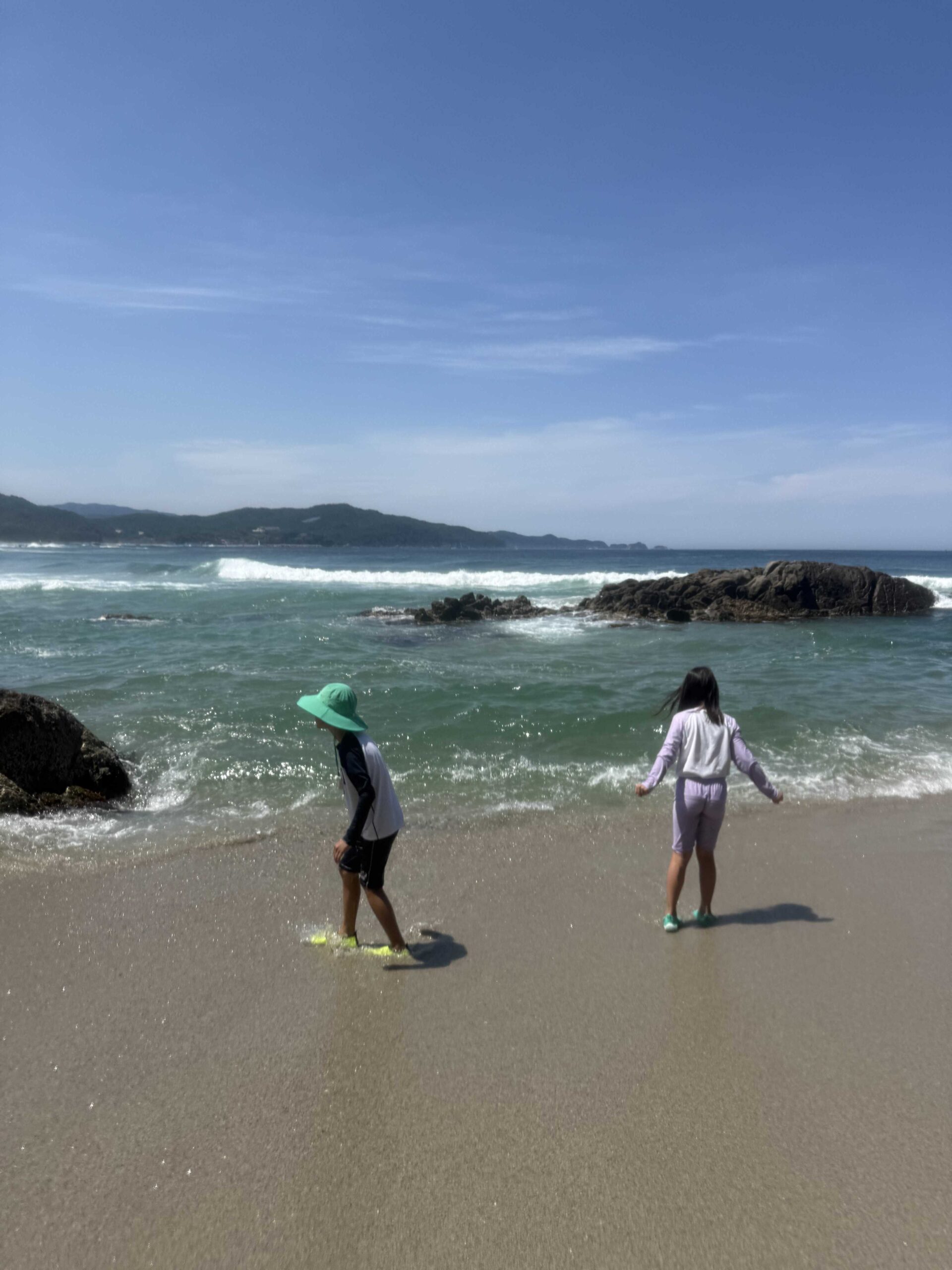 Two kids walking the surf line at Munam Beach Samcheok with rocks and open sea behind