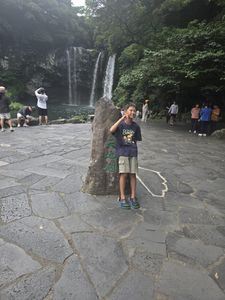 Child posing at the Cheonjiyeon Waterfall marker with the falls behind