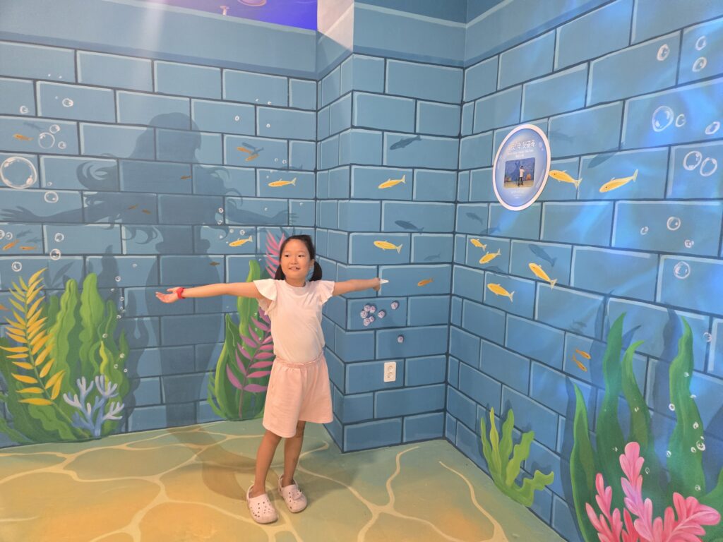 Child posing at a mermaid underwater wall at the Jeju trick art museum