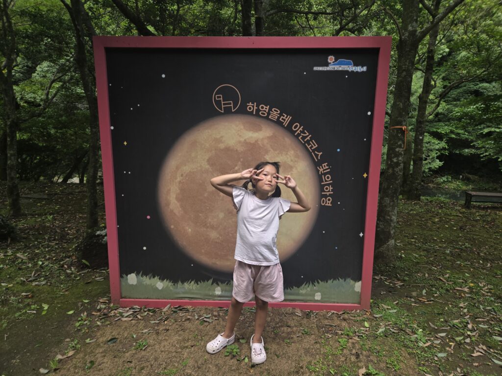 Child posing in front of a giant moon backdrop outside the Jeju trick art museum