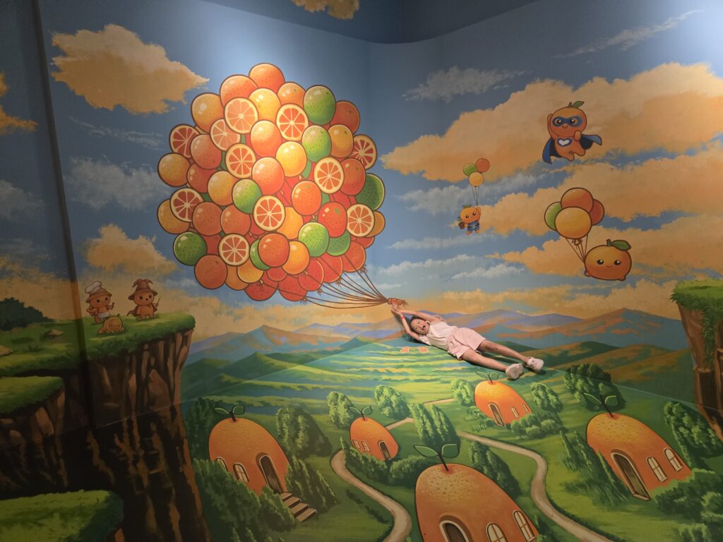 Child posing as if floating with tangerine balloons at the Jeju trick art museum