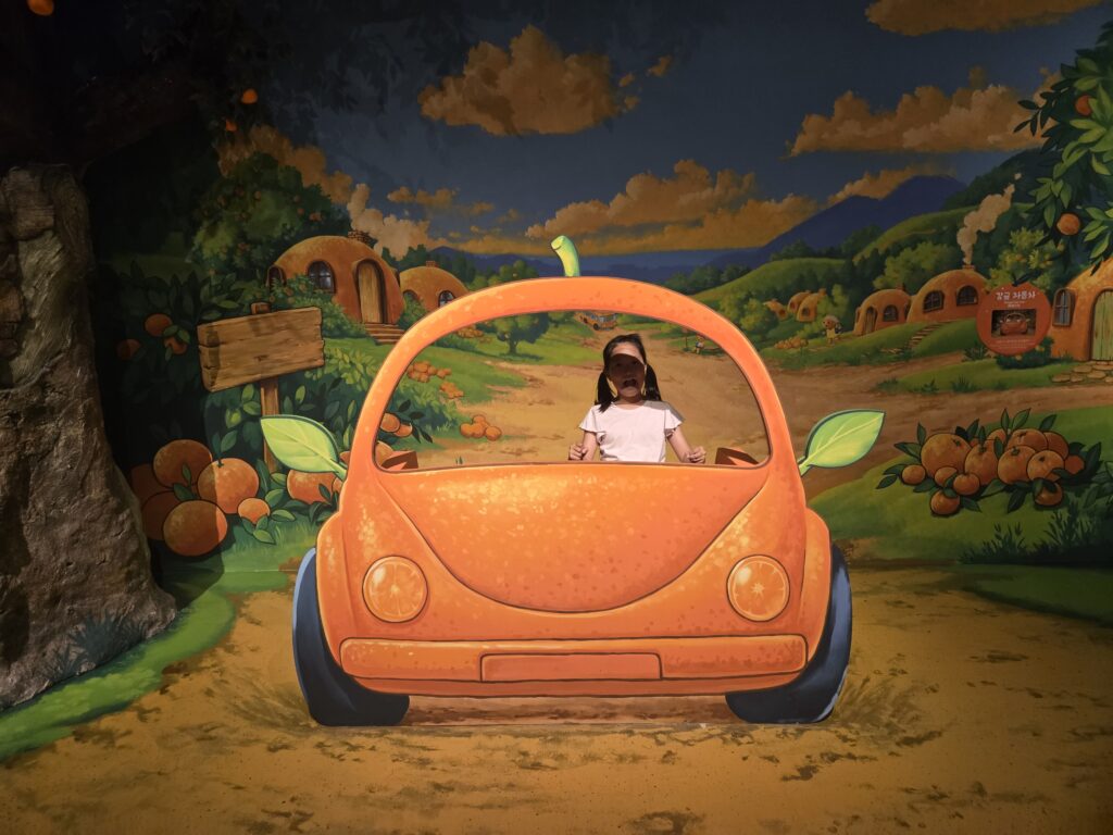 Child driving a painted tangerine car illusion at the Jeju trick art museum