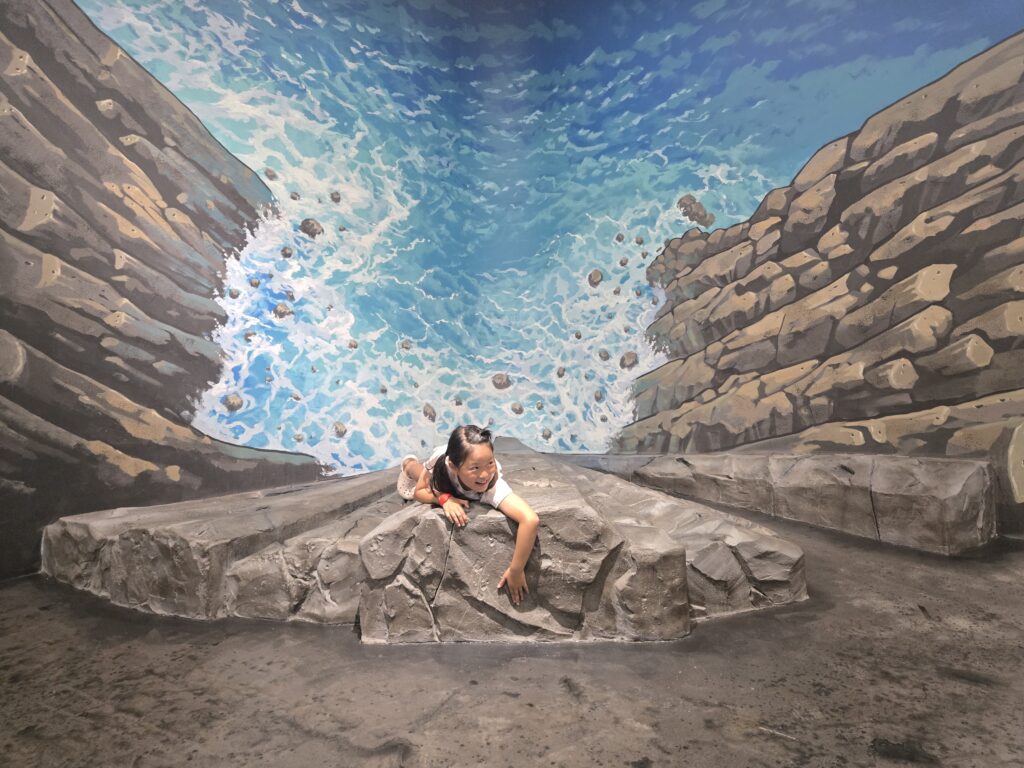 Child climbing a rock in a 3D waterfall illusion at the Jeju trick art museum