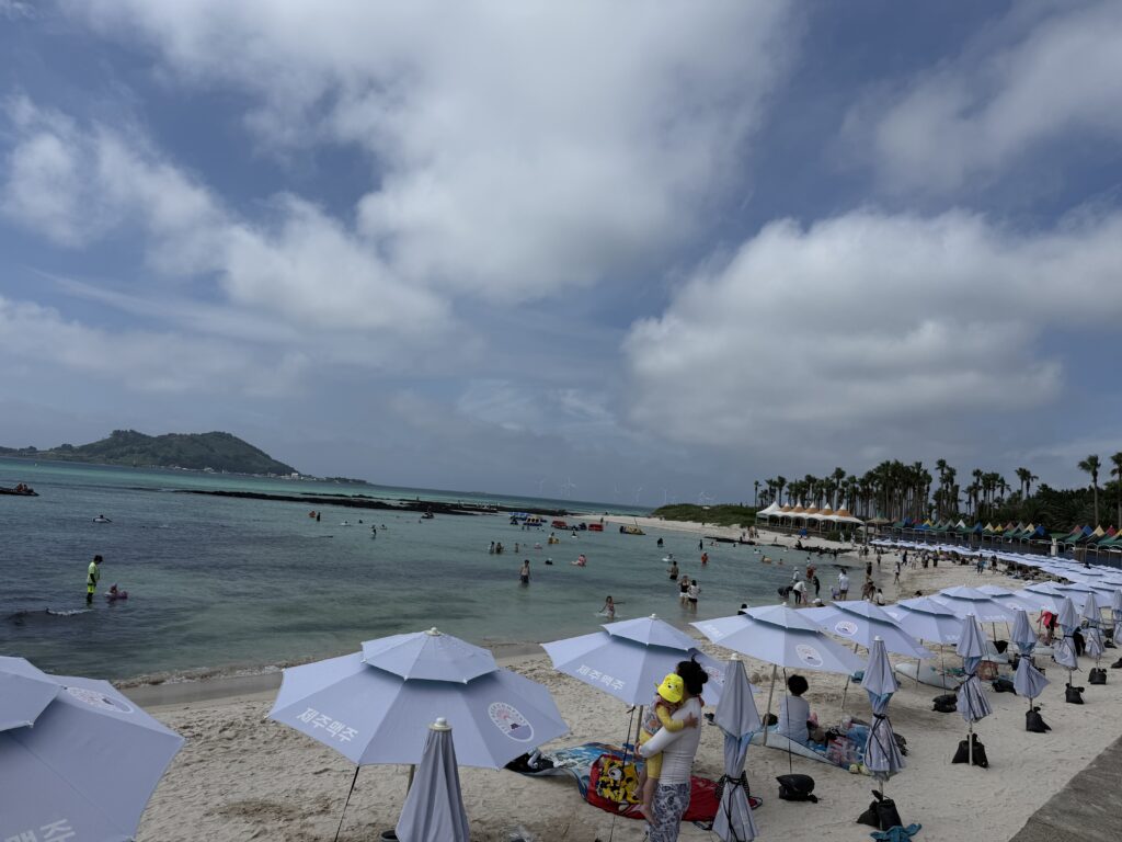 Beach umbrellas and swimmers with an island offshore at Segial Beach Jeju