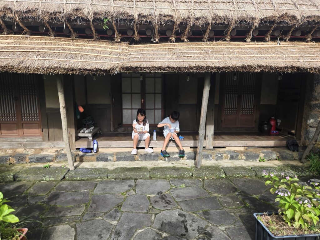 Kids sitting on the wooden porch of the thatched hanok
