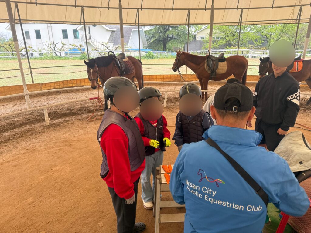 Horseback riding coach briefing kids in helmets and vests at Naepo Camping Square