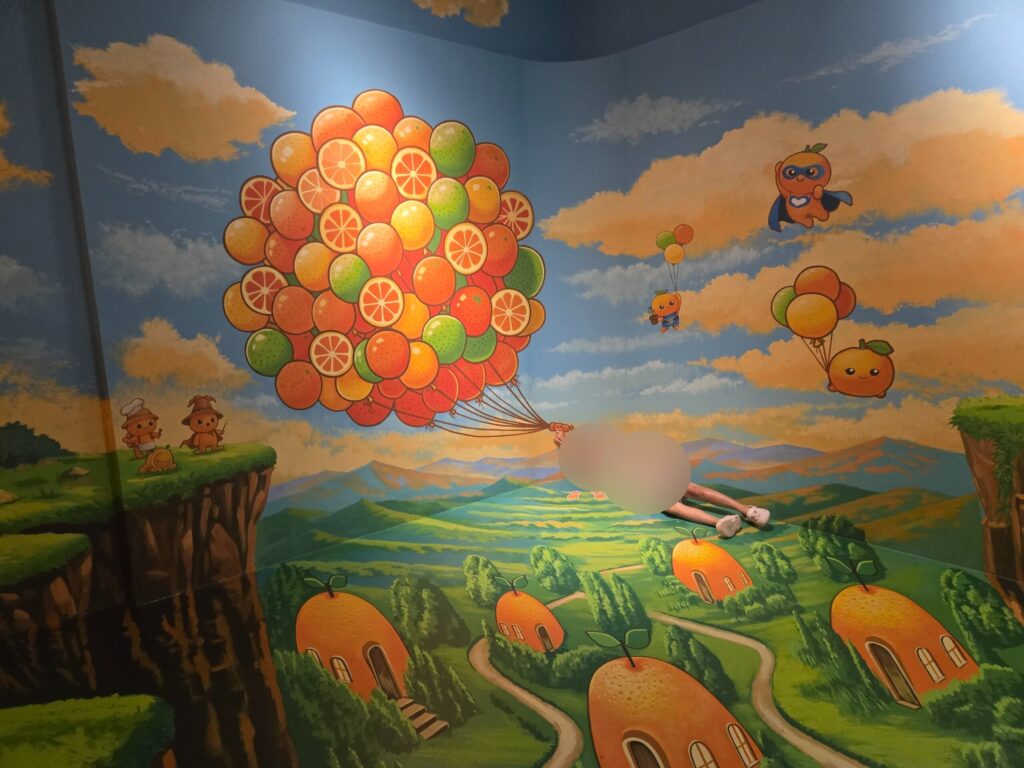 Child posing as if floating with tangerine balloons at the Jeju trick art museum