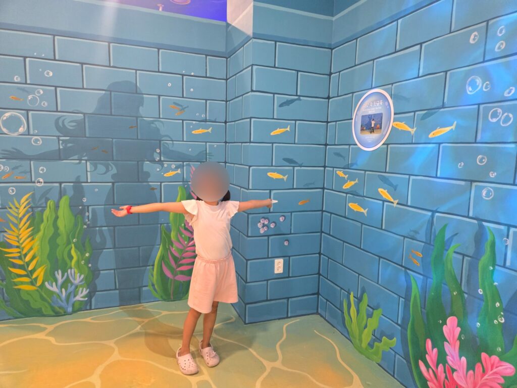 Child posing at a mermaid underwater wall at the Jeju trick art museum