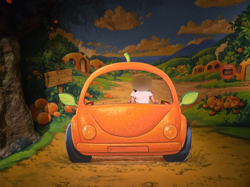 Child driving a painted tangerine car illusion at the Jeju trick art museum