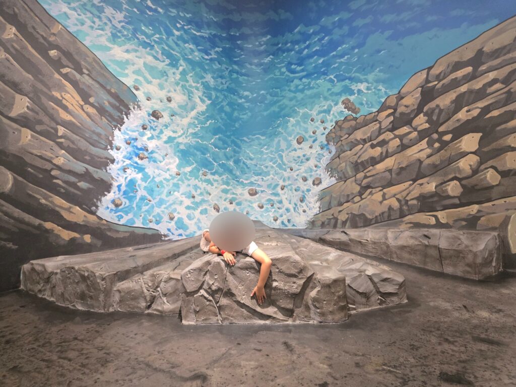 Child climbing a rock in a 3D waterfall illusion at the Jeju trick art museum