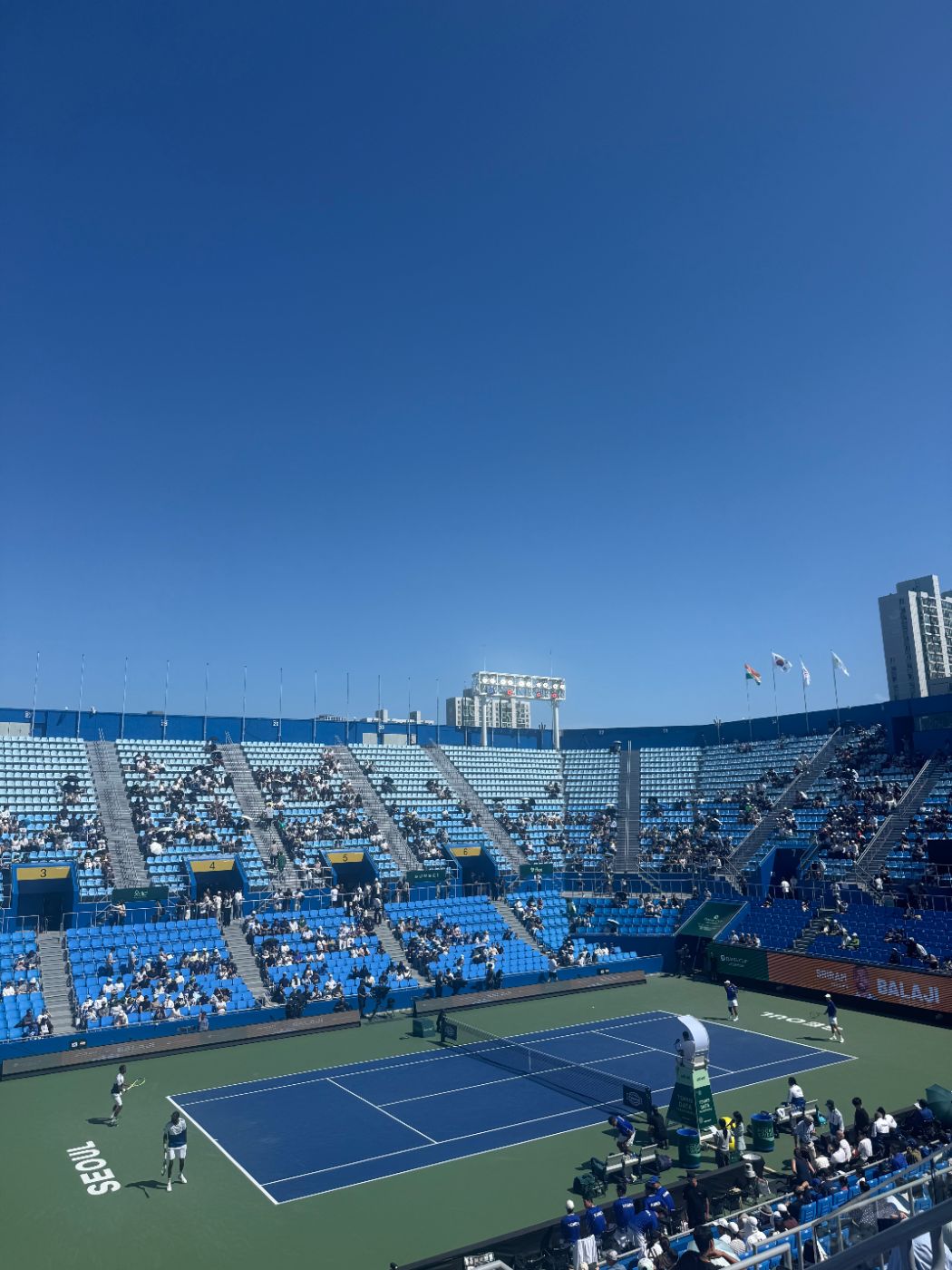 Doubles match in progress at Olympic Tennis Court under a clear blue sky