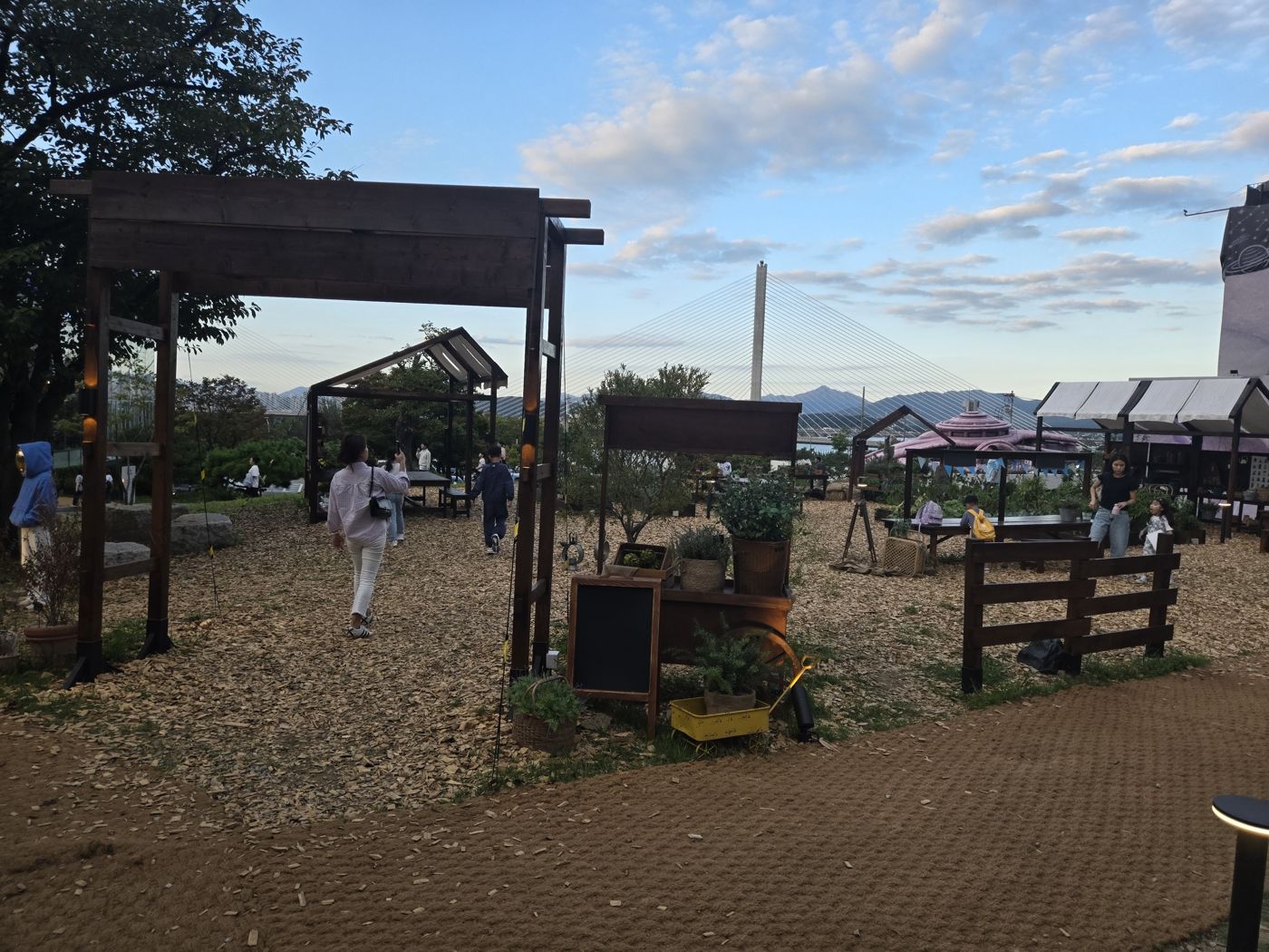 Garden path with wooden frames and huts, the Han River and Godeok-Topyeong Bridge in the distance