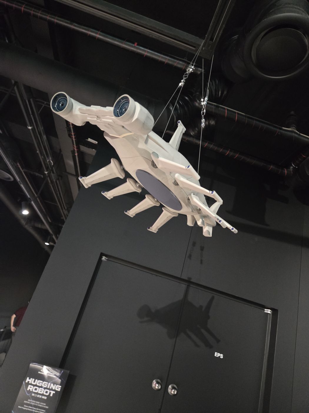Robot model hanging from the ceiling above a Hugging Robot sign in the Robot Arena lobby