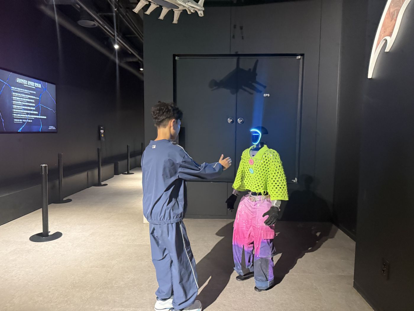 Boy shaking hands with a humanoid robot in a green knit top and pink trousers