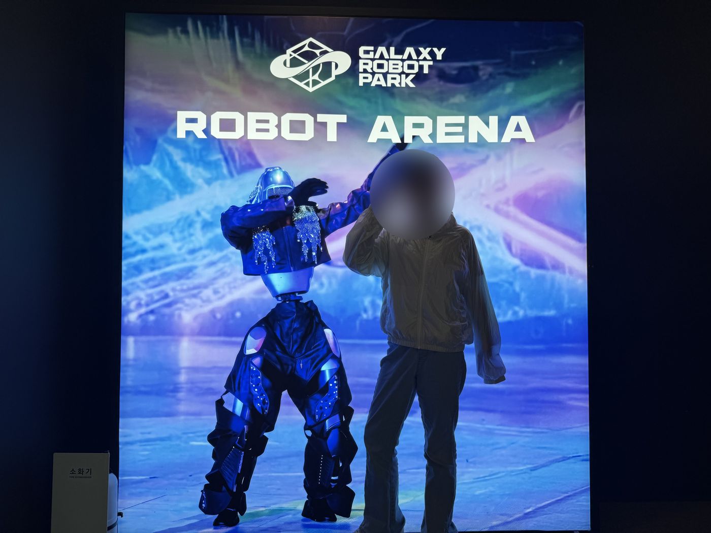 Child posing in front of a Robot Arena photo wall with a dancing robot