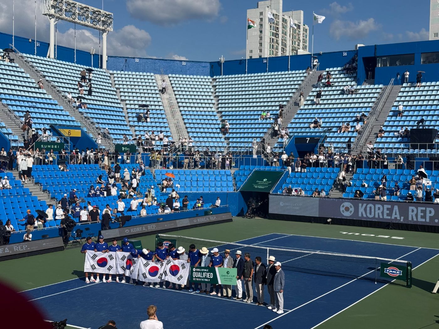 Korean Davis Cup team holding Korean flags and a Qualified banner on court