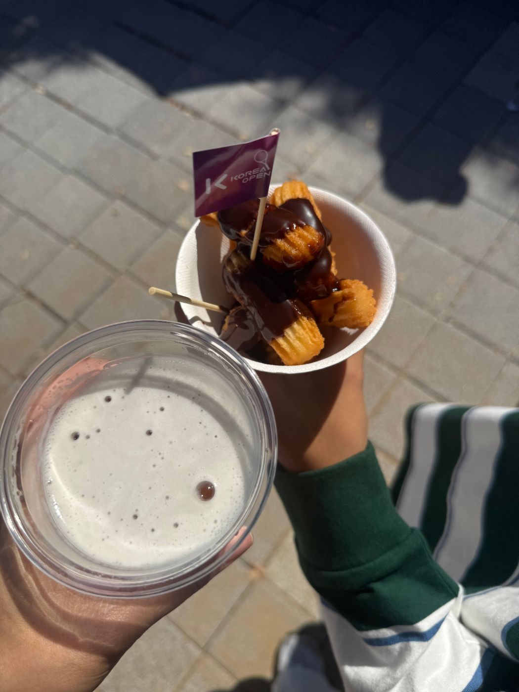 Churros with chocolate sauce in a paper cup with a Korea Open flag, next to a cup of beer