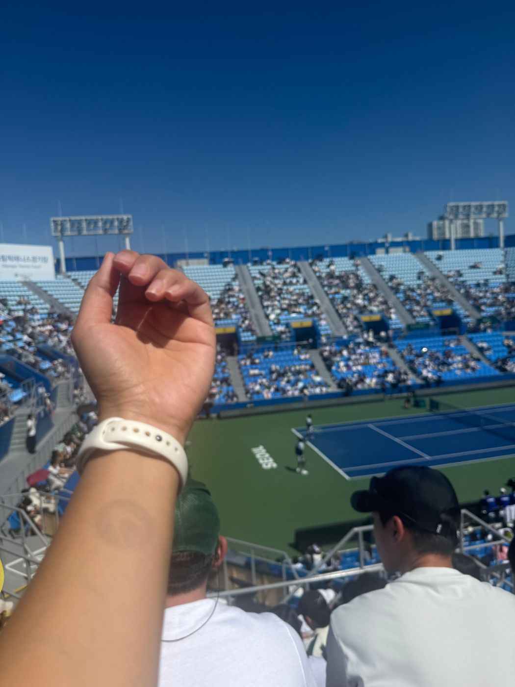 Raised forearm with a round re-entry stamp on the skin, the tennis court and stands behind