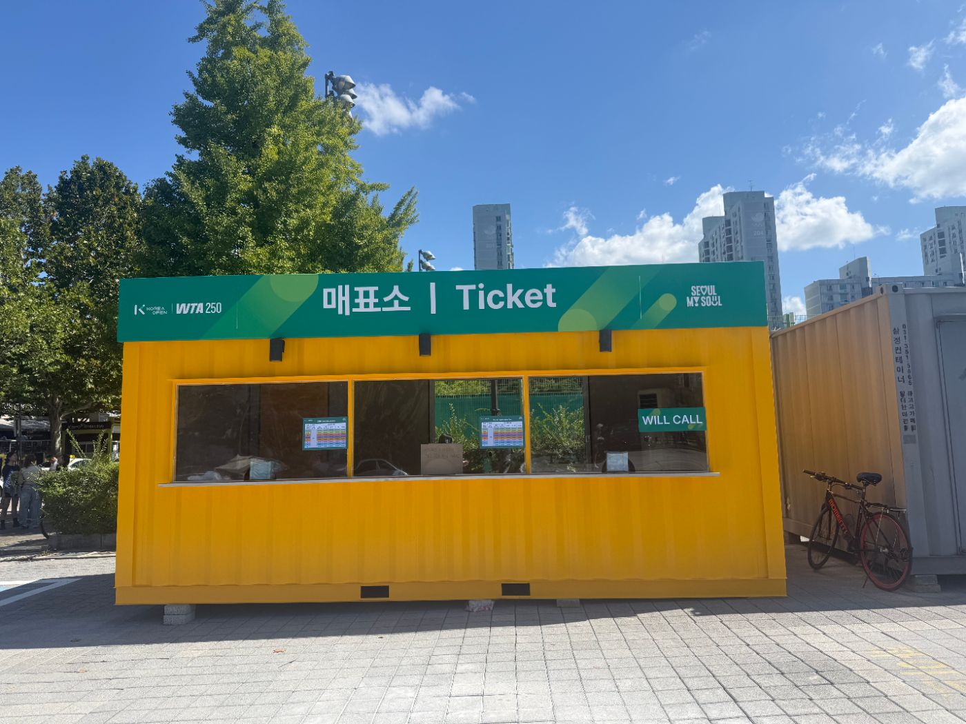 Yellow container ticket booth with a green Ticket sign and a Will Call window
